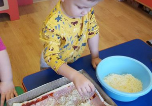 Dzieci sypia serem prawie gotową pizzę.